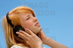 young caucasian teenage girl with red hair singing holding headphones against her ears and listening to music while closing her eyes