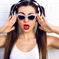 Brunette with dual ponytails and silver sunglasses wears headphones and looks surprised