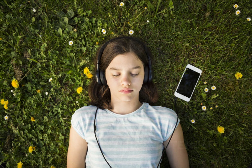 portrait-of-girl-lying-on-meadow-listening-music-with-headphones-and-smartphone-LVF06939