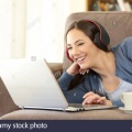 happy-woman-wearing-headphones-watching-media-content-on-a-laptop-lying-on-a-couch-at-home-R8RH3C