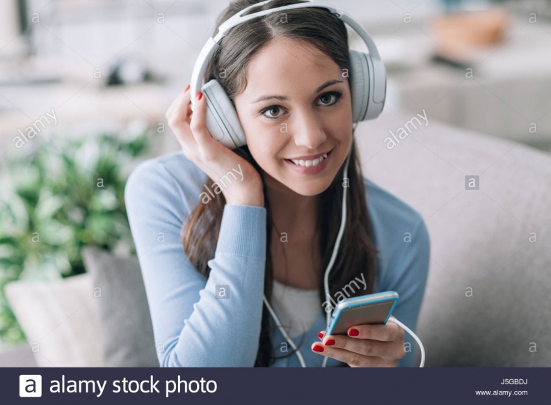 smiling-young-woman-sitting-on-the-sofa-at-home-and-listening-to-music-J5GBDJ.jpg