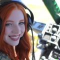A high resolution photo of a cute, smiling young redheaded Caucasian woman wearing a large helicopter headset, detailed, realistic