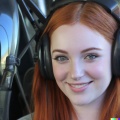 A high resolution photo of a cute, smiling young redheaded Caucasian woman wearing a large helicopter headset, detailed, realistic (2)