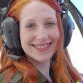 A high resolution photo of a cute, smiling young redheaded Caucasian woman wearing a large helicopter headset, detailed, realistic (3).jpg