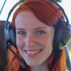 A high resolution photo of a cute, smiling young redheaded Caucasian woman wearing a large helicopter headset, detailed, realistic (6)