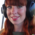 A high resolution photo of a cute, smiling young redheaded Caucasian woman with bangs wearing a large helicopter headset, detailed, realistic.jpg