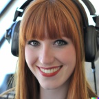 A high resolution photo of a skinny, cute, smiling young redheaded Caucasian woman with bangs wearing a large helicopter headset, detailed, realistic (2)