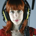 A high resolution photo of a skinny, shy young redheaded woman wearing a large helicopter headset, detailed, realistic